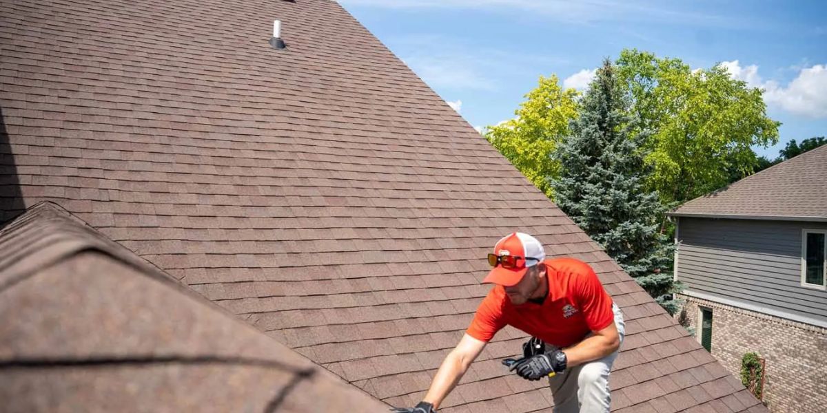 A man in a red shirt performing maintenance work on a roof, emphasizing the importance of regular professional services.