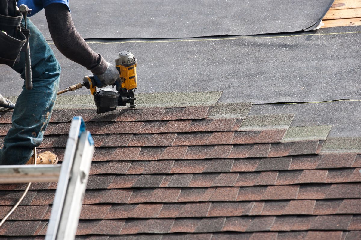 A man uses a nail gun while working on a roof during a roof replacement project.