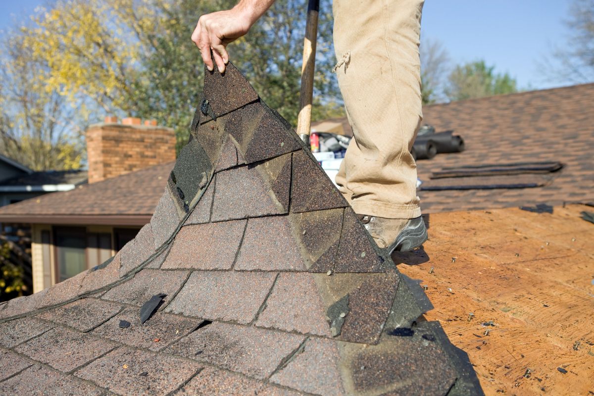  A man wearing a hard hat and yellow safety vest is engaged in roof repairs, highlighting the importance of safety in roofing.
