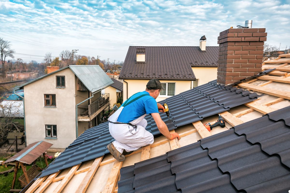 A man installs metal roofing on a sloped roof, wearing safety gear and focused on his work. 