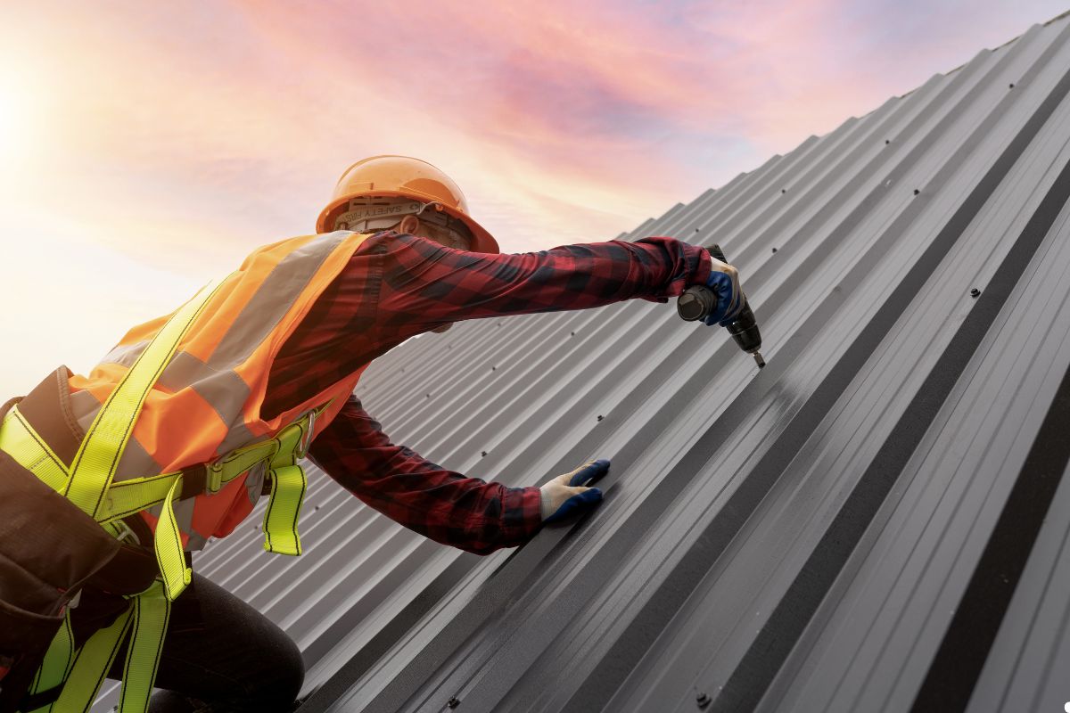 A man in safety gear is installing panels on a metal roof, demonstrating proper safety practices while working at height.