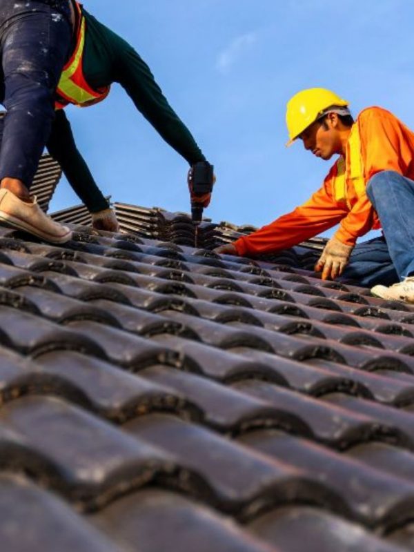 Two men laboring on a roof beneath a clear blue sky, depicting a roofing construction service located in Brittain Rd, Akron.