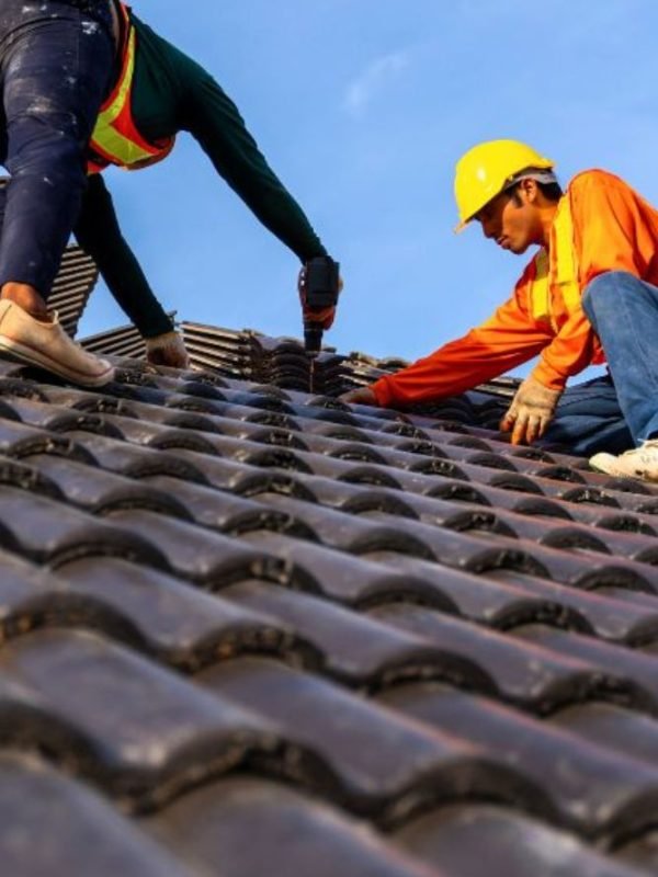 Two men laboring on a roof beneath a clear blue sky, depicting a roofing construction service located in Brittain Rd, Akron.